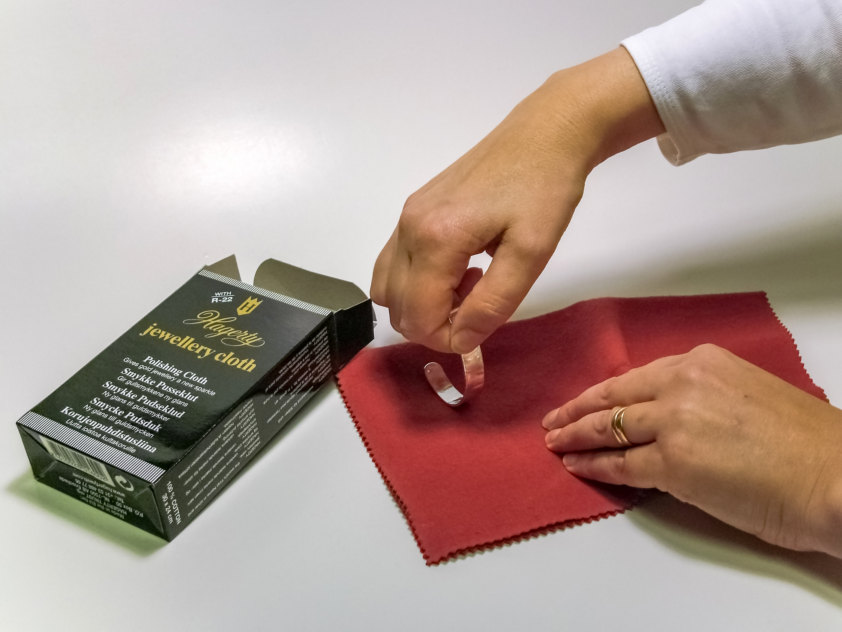Hands polishing a small silver item with a soft cloth.